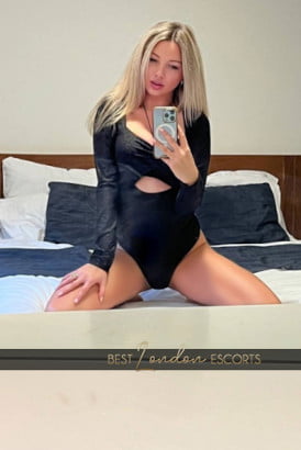 Busty blonde kneeling on a bed and taking a selfie photo